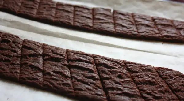 Två rader med sega chokladsnittar på bakplåtspapper, redo att gräddas.