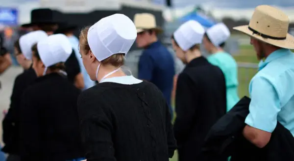 Människor i traditionella kläder, som påminner om amish i Sverige, med vita hättor och hattar.