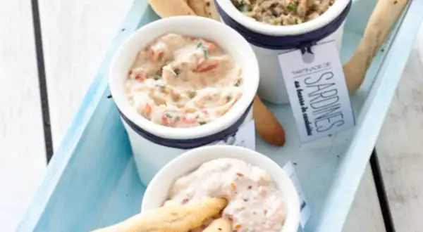 Trois ramequins de rillettes de la mer, dont une tartinade de sardines, présentés sur un plateau bleu avec des gressins.