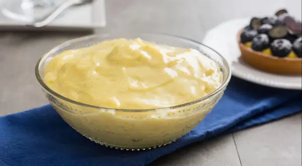 Cremige, vanilleschotenhaltige Crema Pasticcera in einer Glasschüssel, daneben ein Blaubeer-Törtchen.