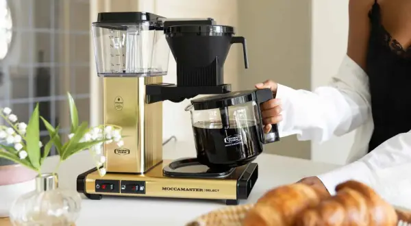 En gyllene Moccamaster brygger kaffe, perfekt för en italiensk frukost med nybakade croissanter.