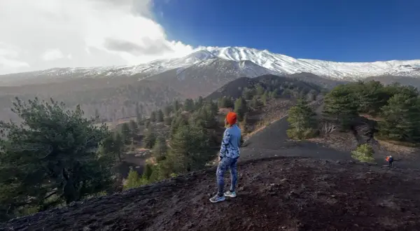 Kobieta w pomarańczowej czapce podziwia majestatyczny wulkan Etna pokryty śniegiem.