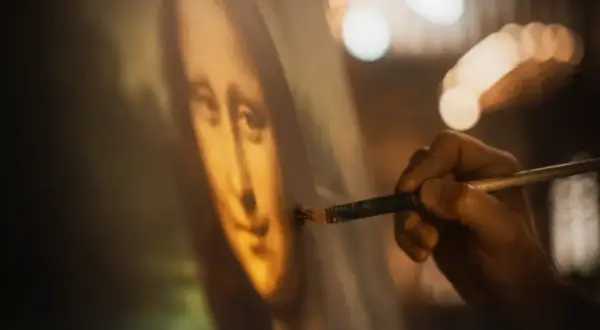 Dłoń artysty dopracowuje słynny obraz Leonarda da Vinci, Mona Lisę, dodając ostatnie pociągnięcia pędzlem.