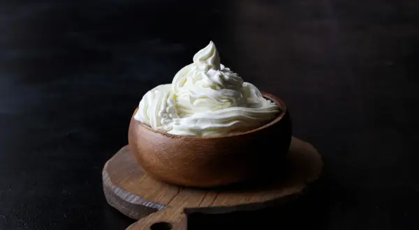 Kremowy mascarpone w drewnianej miseczce, idealny do deserów. Warto sprawdzić mascarpone kcal przed przygotowaniem słodkości.