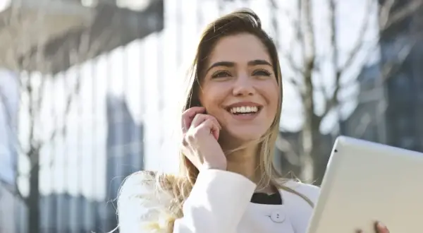 Donna sorridente con tablet, forse sta per uscire prima dal lavoro senza permesso, con un'aria di gioia e libertà.