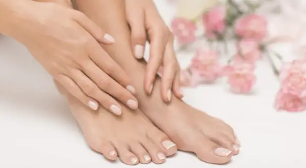 Pieds et mains soignés avec une french pedicure parfaite, entourés de fleurs roses délicates.