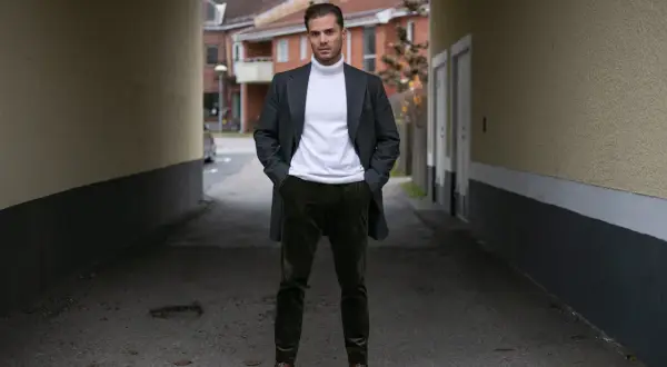 Mężczyzna w eleganckim płaszczu i białym golfie, dumnie prezentuje swoje stylowe sztruksy.