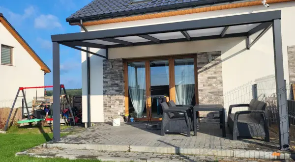 Nowoczesna pergola z poliwęglanowym dachem chroni taras z meblami. Idealne miejsce na relaks.
