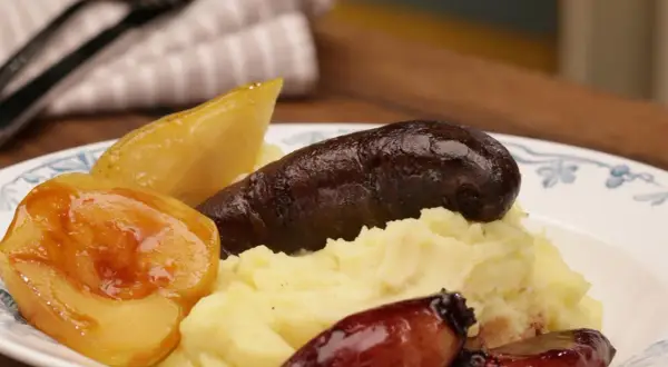 Herzhaftes Gericht mit Kartoffelpüree, dunkler Wurst, karamellisierten Zwiebeln und Birnenstücken – eine köstliche Kombination aus Himmel und Erde.