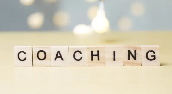 Drewniane klocki z literami układają słowo "COACHING". To właśnie kim jest coach – osoba wspierająca rozwój.
