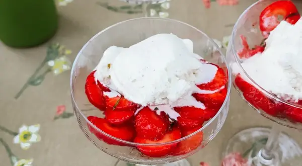 Två glas med limemarinerade jordgubbar och vaniljglass på ett blommigt duk.
