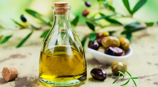 Olio di sansa in bottiglia di vetro, con olive miste e rametto di rosmarino. Un condimento versatile, l'olio di sansa è commestibile e perfetto per ogni piatto.