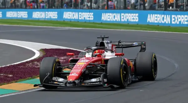Un'auto di F1 in gara, con livrea rossa Ferrari, sfreccia in curva. La pubblicità "American Express" fa da sfondo a questa emozione da vedere in TV.