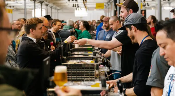 Folla a un evento di degustazione di birra a Mikkeller Copenhagen. Un uomo porge un bicchiere di birra scura.