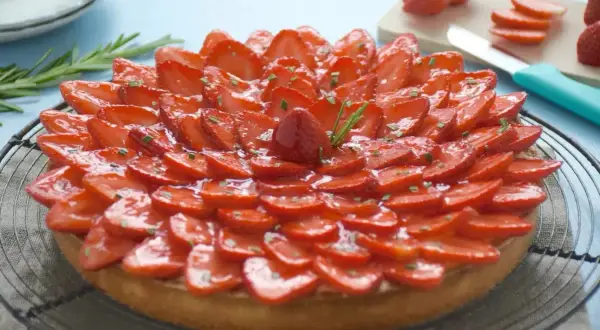 Tarte fraise aux fraises fraîches, joliment disposées en rosace sur une pâte dorée, garnie de quelques brins de romarin.