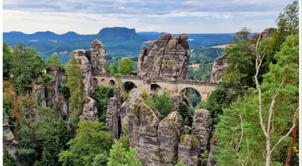 Kamienny most Bastei w górach Saksonii, łączący skalne baszty pośród zielonych lasów i malowniczych krajobrazów.