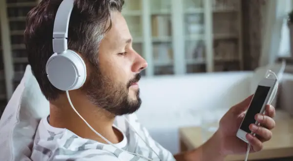 Mężczyzna w słuchawkach relaksuje się, słuchając muzyki na telefonie. Idealny sposób na darmową muzykę na telefon!