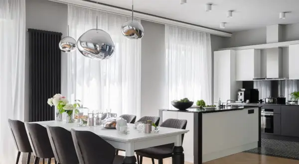 Elegancki styl glamour salon z kuchnią. Nowoczesne lampy, biała wyspa kuchenna i stół z szarymi krzesłami tworzą spójną całość.