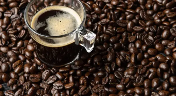 Una taza de café oscuro con espuma, rodeada de granos de café tostados. Dicen que el café es afrodisiaco, ¿será cierto?