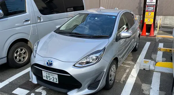 Srebrny samochód na parkingu w Japonii, gdzie obowiązuje ruch lewostronny. Obok stoi srebrny van.
