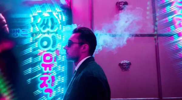 Man exhales smoke in front of vibrant neon signs, a cool example of led light photography ideas.