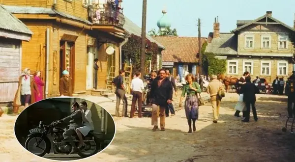 Scena z filmu "Znachor" kręcona w malowniczej wsi. W tle drewniane domy, a na pierwszym planie para na motocyklu.