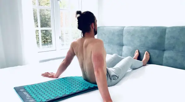 Man zit op een spijkermat, genietend van de ontspanning. De vraag is: hoe lang op spijkermat liggen voor optimaal effect?