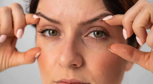 Dita che sollevano la pelle per mostrare come truccare gli occhi con palpebre cadenti, creando un effetto lifting.
