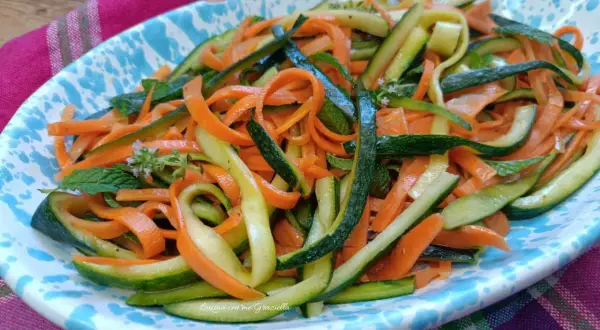 Deliziose zucchine alla julienne con carote, guarnite con menta fresca, servite su un piatto colorato.