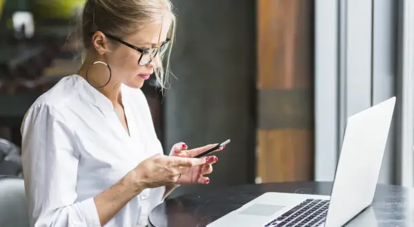 Kobieta w okularach i białej koszuli korzysta z telefonu, obok leży laptop. Upewnij się, że Twoje datezone połączenie nie jest prywatne.