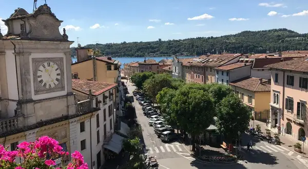 Vista dall'alto di Salò, con il lago sullo sfondo. Un orologio segna l'ora su un edificio storico.