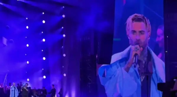 Quebonafide koncert na żywo. Artysta śpiewa do mikrofonu, a jego twarz widać na wielkim ekranie. Tłum szaleje.