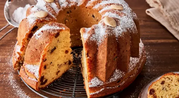 Ein köstlicher Gugelhupf-Kuchen mit Rosinen und Mandeln, bestäubt mit Puderzucker. Der Gugelhupf-Kuchen geht nicht aus der Form, aber ein Stück wurde bereits herausgeschnitten.