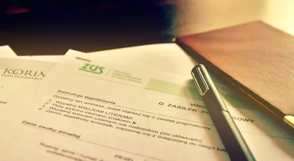 Wniosek o zasiłek pogrzebowy ZUS. Dokumenty i długopis na biurku sugerują formalności związane ze śmiercią za granicą.