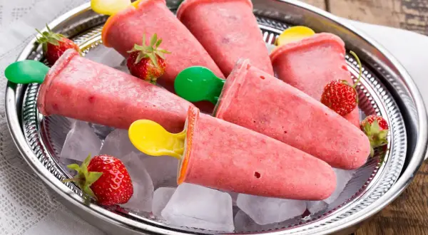 Erfrischendes Erdbeer-Eis am Stiel selber machen. Auf einem Silbertablett mit Eiswürfeln und frischen Erdbeeren serviert.