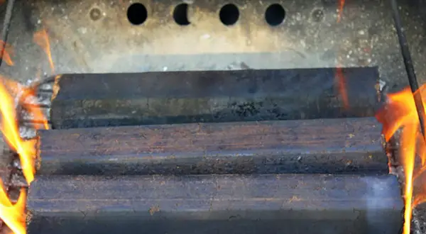 Drei Braunkohlebriketts brennen im Kaminofen. Die Flammen lodern um die Briketts.