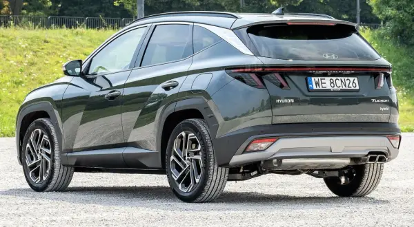Tylna część ciemnozielonego Hyundaia Tucsona hybrydowego na żwirowej drodze. Wiele osób szuka hyundai tucson opinie przed zakupem.