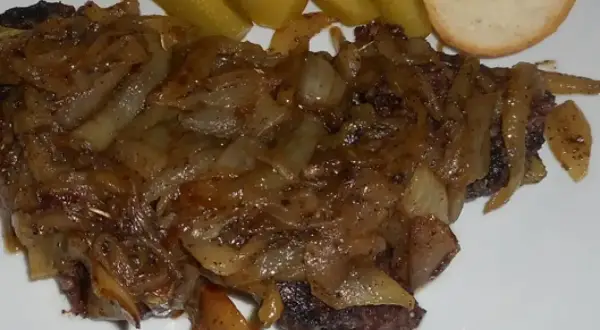 Pyszna kaszanka z patelni, duszona z cebulką, podana z ogórkiem kiszonym i kromką chleba.