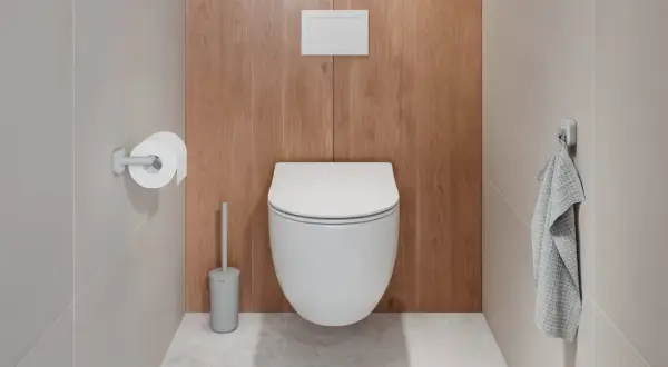 Uchwyt na papier toaletowy zamontowany na wysokości ok. 65 cm od podłogi, obok nowoczesnej toalety.