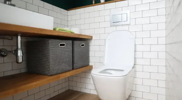 Nowa deska wolnoopadająca do toalety. W łazience białe kafelki, drewniane półki z koszami i nowoczesna miska WC.