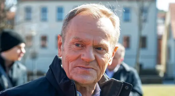 Tusk, z widocznym wiekiem, w ciemnej kurtce, na tle budynków.