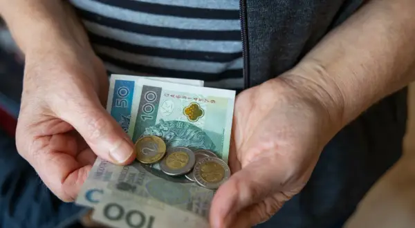 Dłonie trzymają polskie banknoty i monety. Nadzieja na waloryzację rent i emerytur 2026.