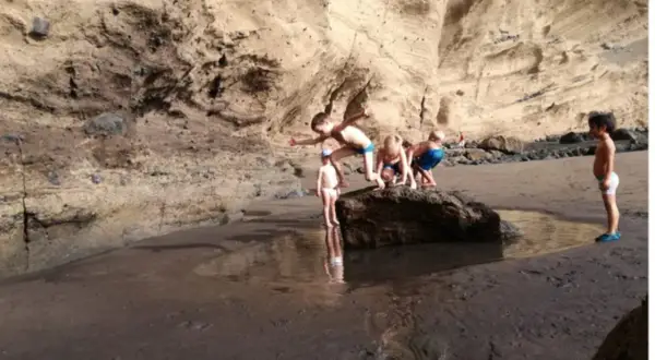 Un grupo de niños exploran una poza en la playa, rodeados de acantilados rocosos.