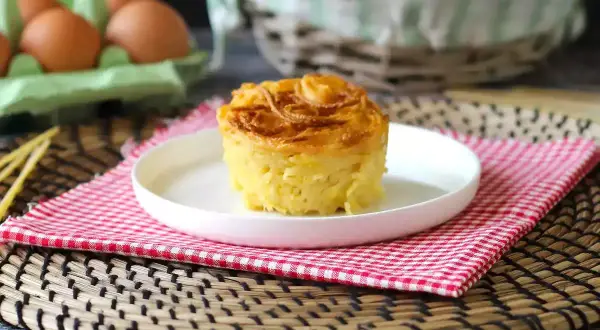 En gyllene, krispig makaronipudding på en vit tallrik, perfekt för ett maskros recept. Ägg i bakgrunden.