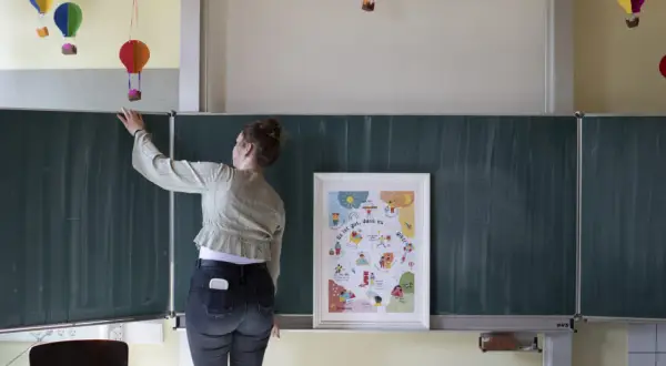 Lehrerin vor Tafel mit Poster "Es ist gut, dass es mich gibt!". Bunte Ballons hängen von der Decke. Ein Beispiel für heilende Klassenzimmer.