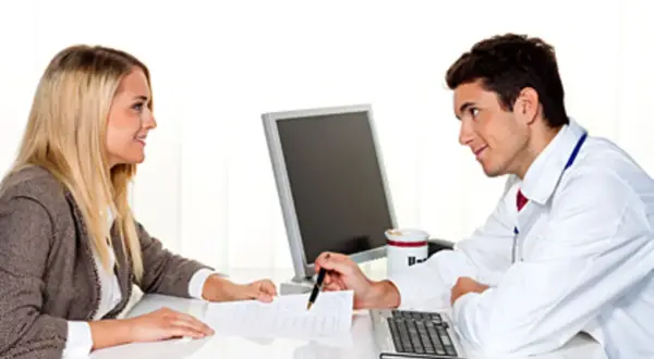 Arzt erklärt einer Frau, was passiert, wenn man die private Krankenversicherung nicht bezahlt. Sie besprechen Dokumente am Schreibtisch.