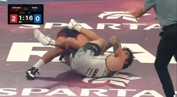 Intens kamp i catch wrestling. En brottare har den andra i ett grepp på mattan.