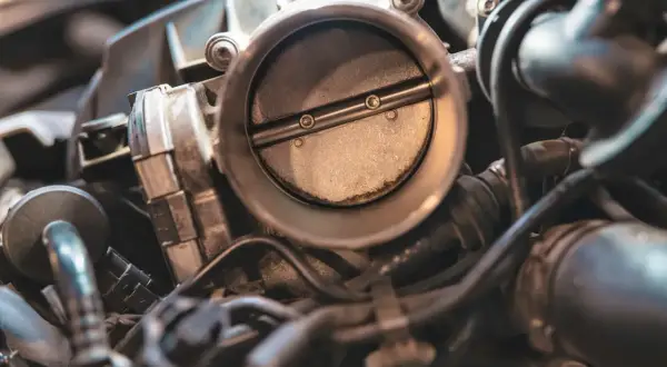 Gros plan sur un boîtier papillon reste ouvert sur un moteur diesel. La lumière éclaire la pièce métallique et les conduits environnants.