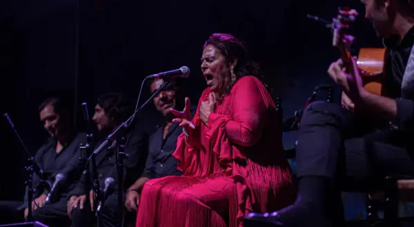 Una cantante colombiana flamenco, con un vestido rojo vibrante, canta apasionadamente acompañada por guitarristas.