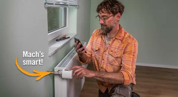 Mann mit Smartphone installiert smarten Thermostat an Heizkörper. Einfach das Thermostat wechseln und Energie sparen.